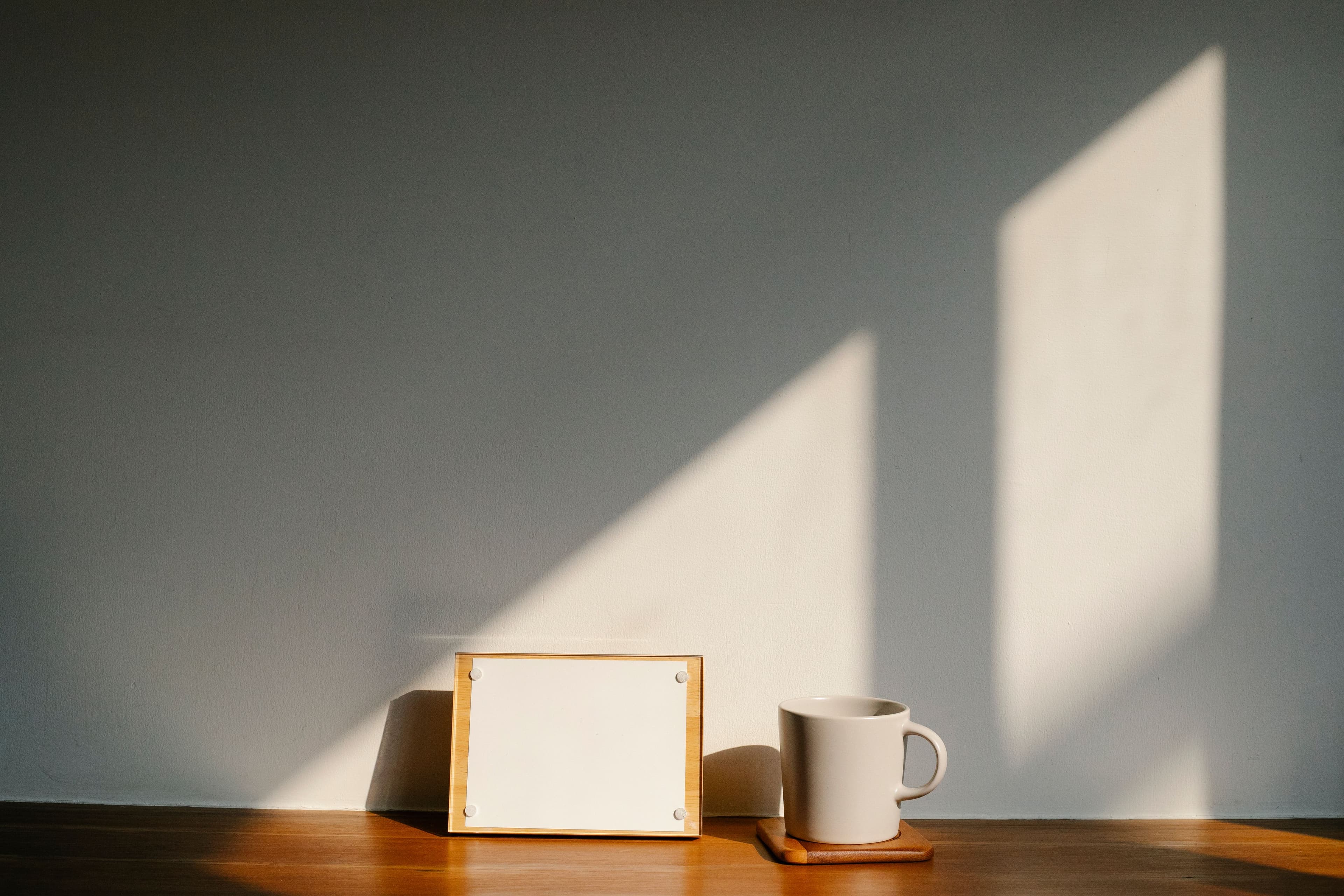 Morning light falling across a wall above a desk with a mug and a picture frame.
