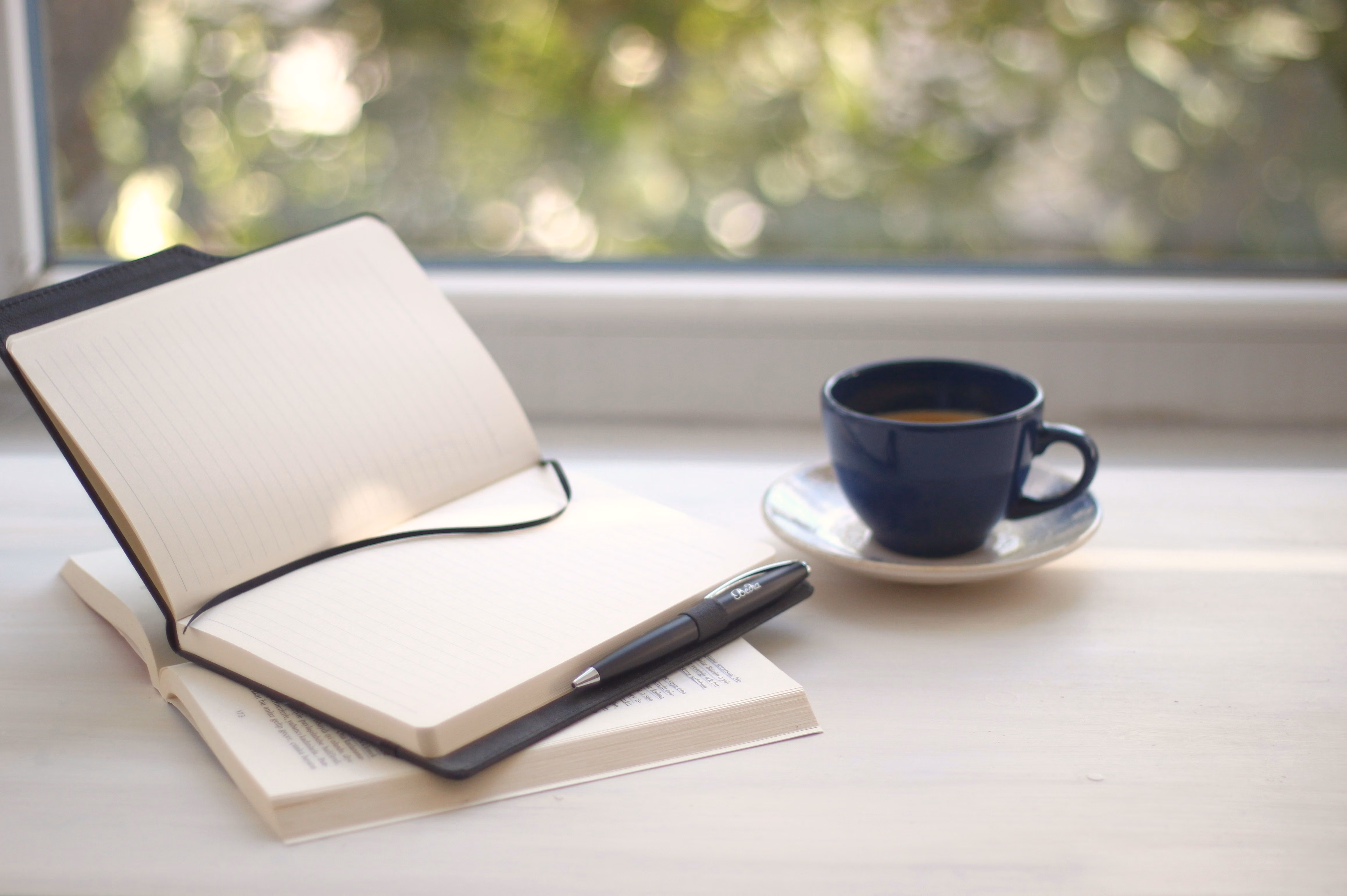 An open blank notebook and a cup of coffee on a windowsill in morning light.